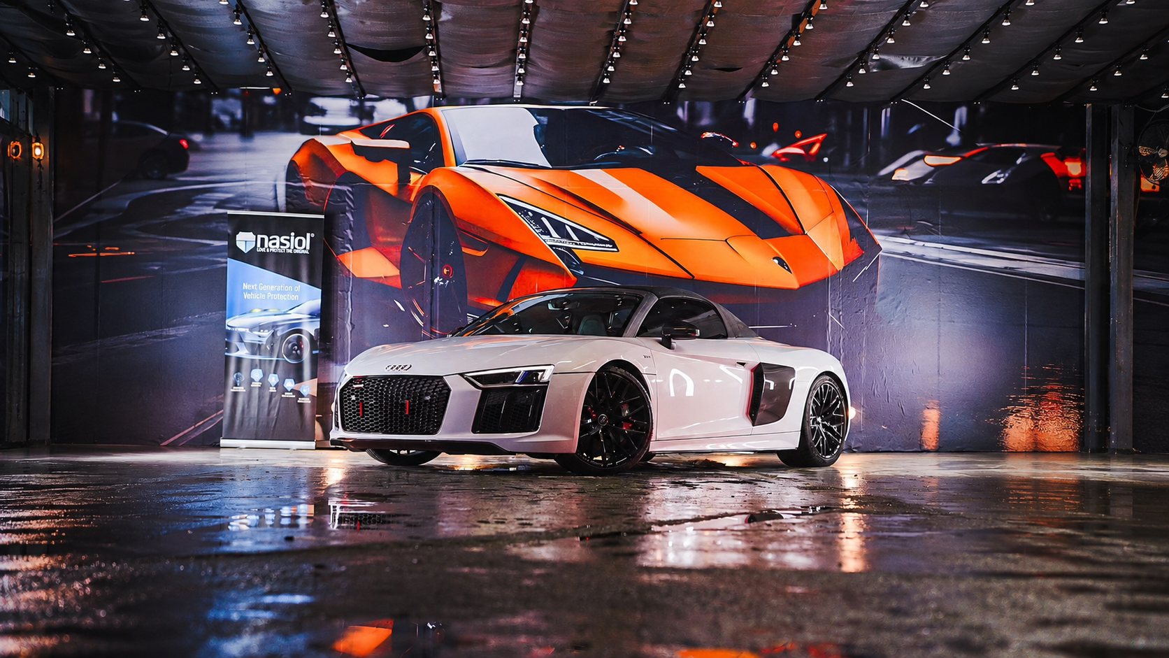 White Audi R8 Spyder on the wet studio floor at Adonai Auto Spa, supercar mural behind